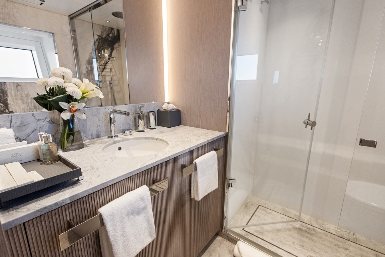 Shower aboard Benetti 133 “Contigo” with glass enclosure, rainfall showerhead, and marble accents.