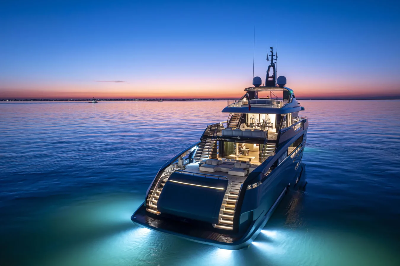Aft view of the Ocean King DOGE 400 explorer yacht at sunset, illuminated while cruising on calm water with exterior lights.