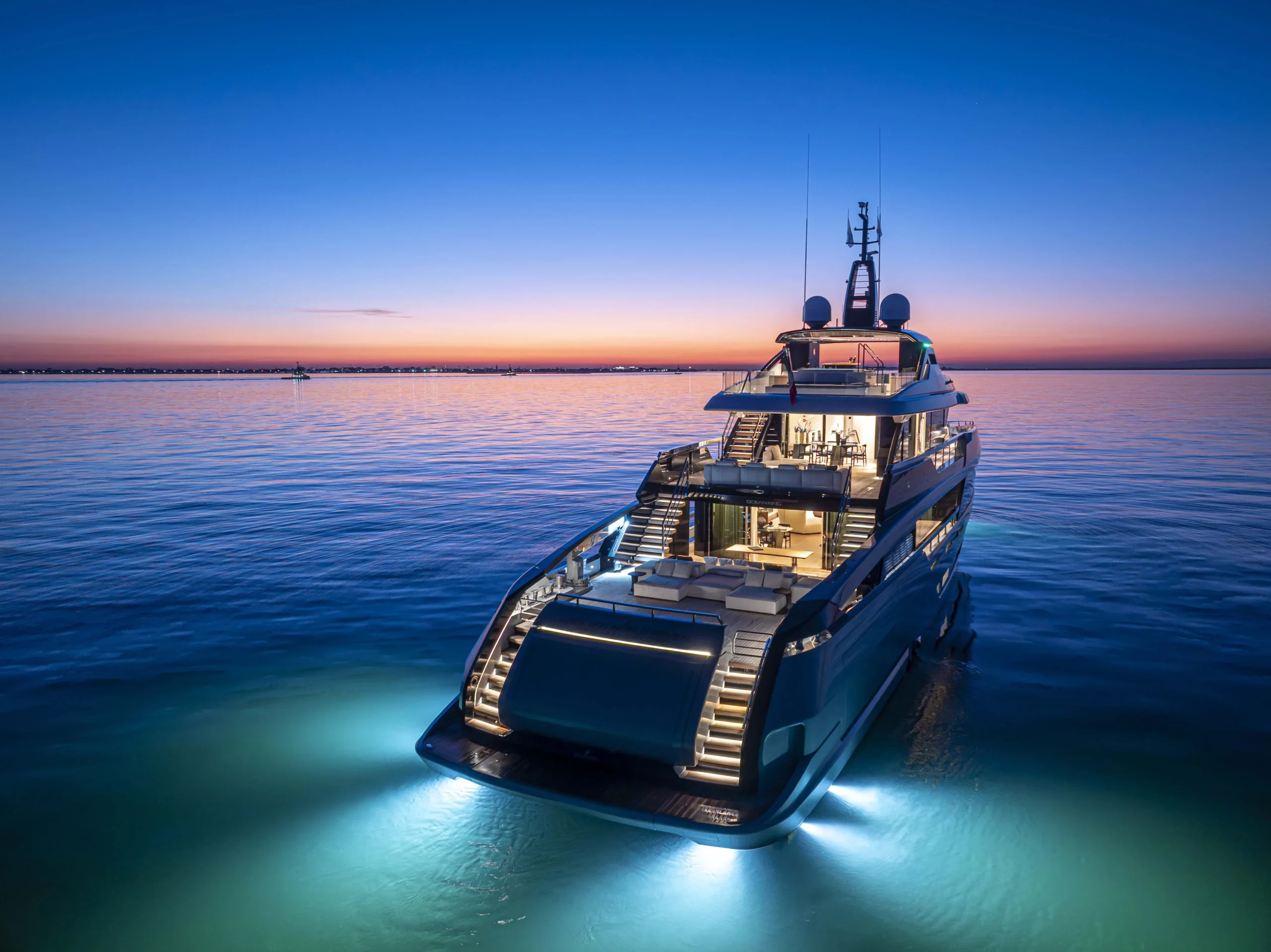 Aft view of the Ocean King DOGE 400 explorer yacht at sunset, illuminated while cruising on calm water with exterior lights.