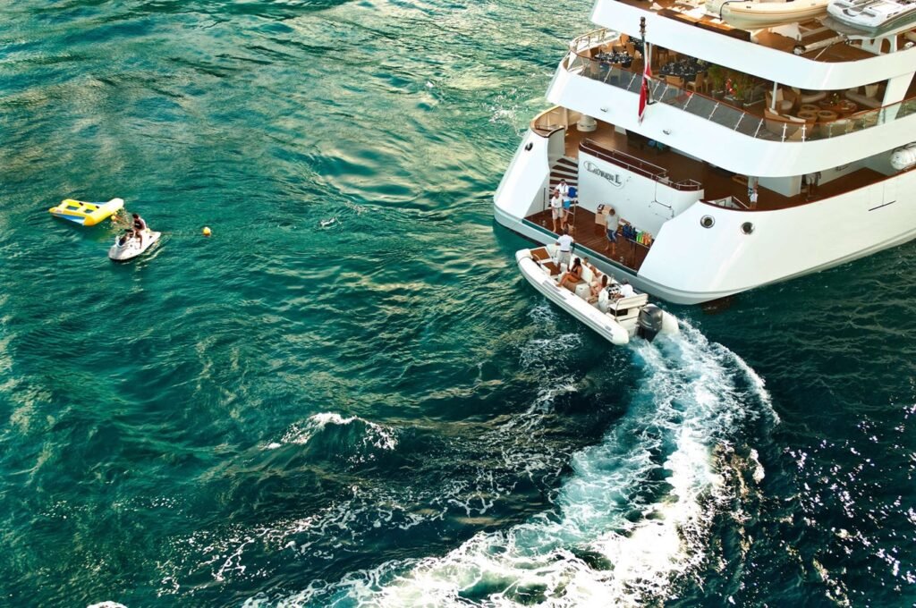 The Cassens-Werft PV Lauren L Yacht on turquoise water, with people on deck and two floating nearby on a yellow float.