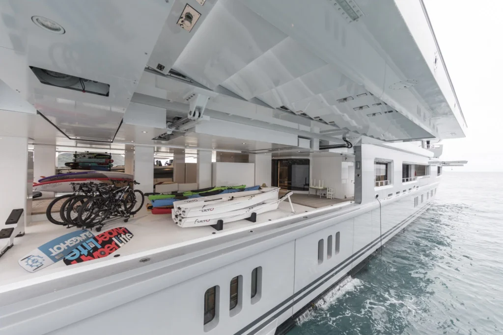 Open yacht garage on Abeking Rasmussen Cloudbreak yacht for charter: surfboards, bikes, kayaks, and boat by calm water.