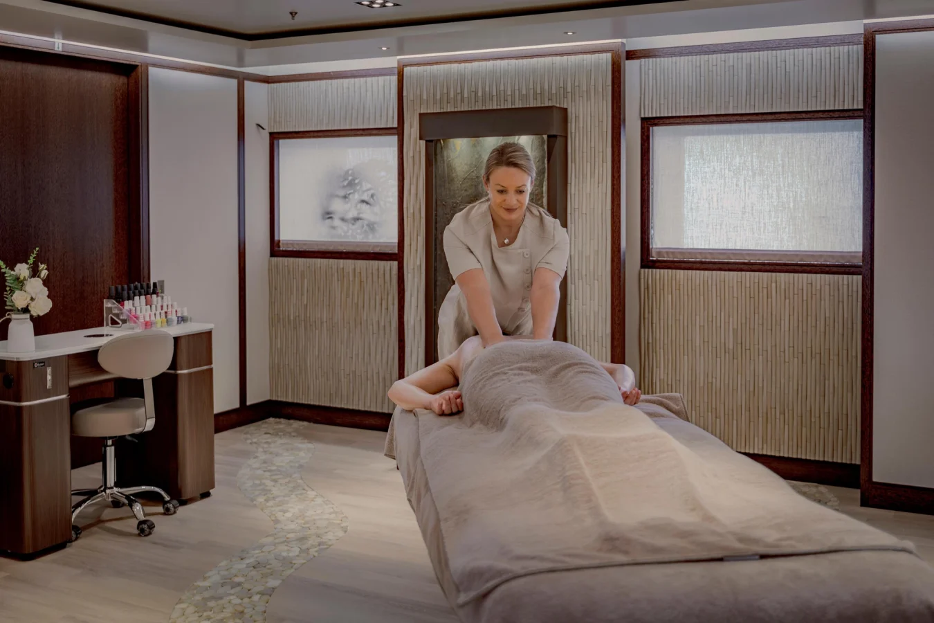 A spa therapist gives a massage to a client lying face down on a massage table in a modern, serene treatment room.