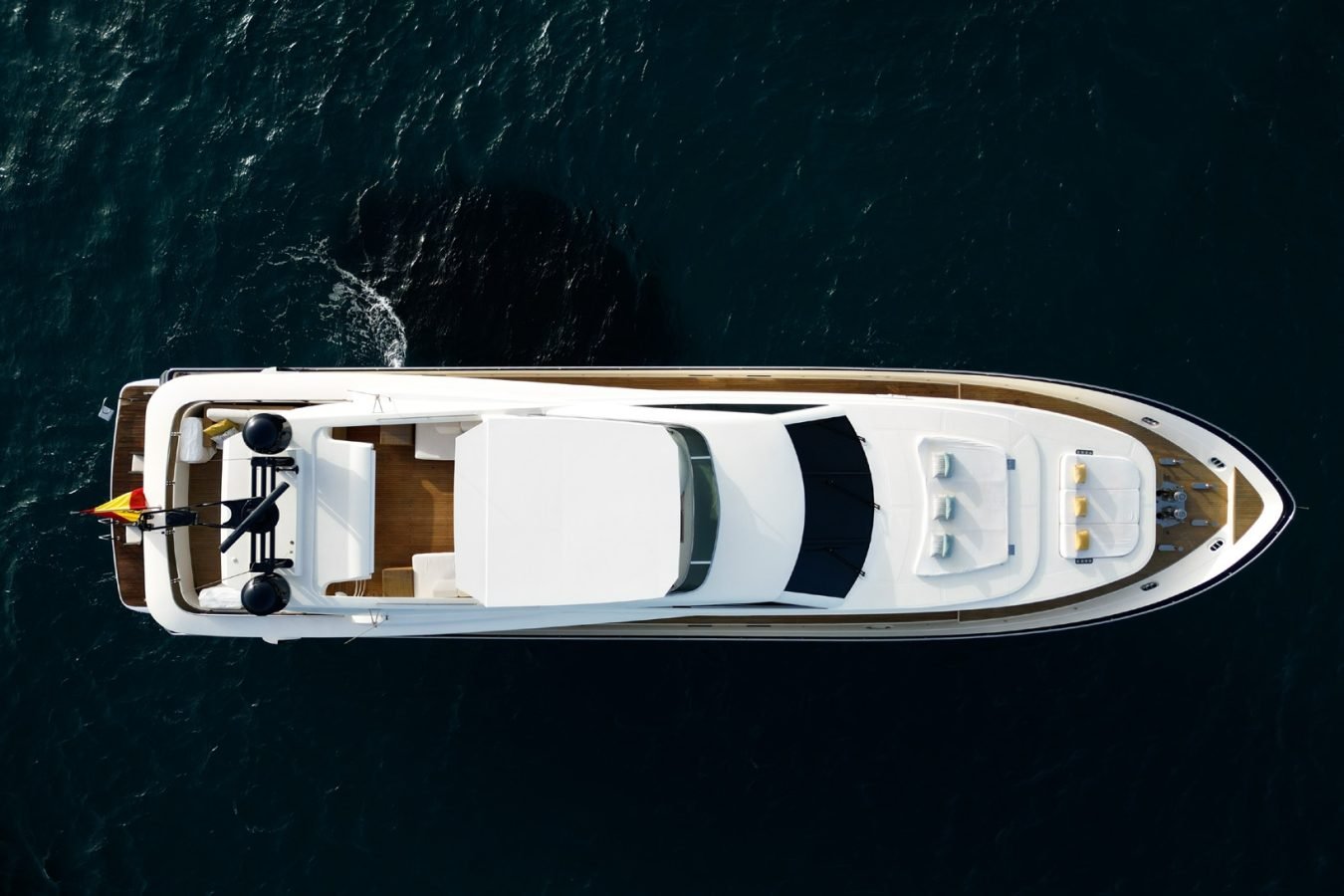 Aerial view of Astondoa 102 GLX My Kirios Yacht For Charter, with a person at the back near a flag on dark blue water.