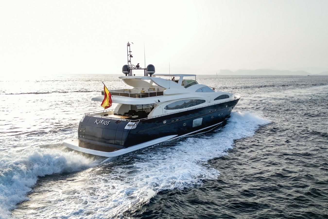 The Astondoa 102 GLX My Kirios Yacht for charter glides on open water, trailing a foamy wake beneath a hazy sky.