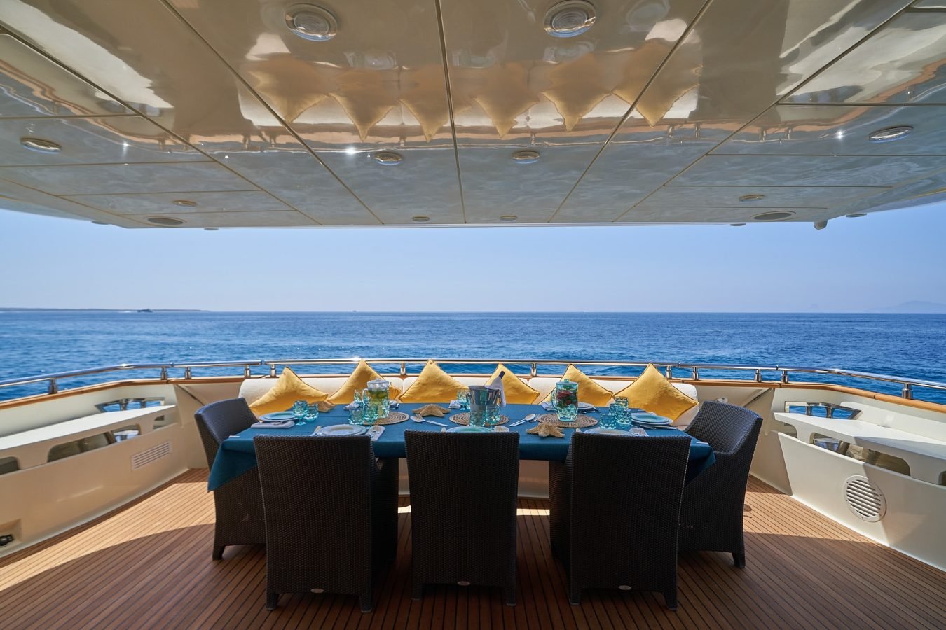 Dining table with yellow pillows overlooks calm blue sea from Astondoa 102 GLX My Kirios Yacht For Charter’s deck.