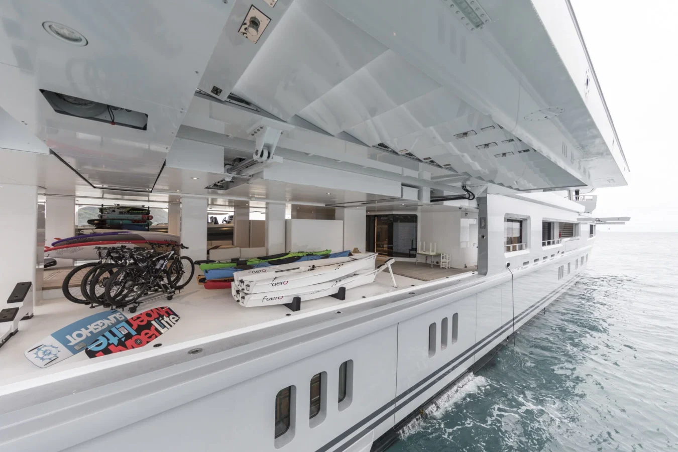 Open yacht garage on Abeking Rasmussen Cloudbreak yacht for charter: surfboards, bikes, kayaks, and boat by calm water.