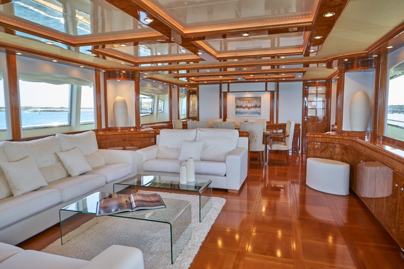 Luxurious Astondoa 102 GLX My Kirios Yacht for Charter features white sofas, glass table, wood paneling, ocean views.