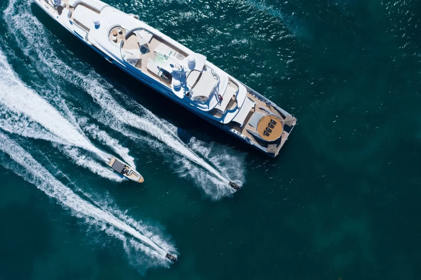 Aerial view of a large white yacht and two small boats creating wakes in deep blue ocean water.