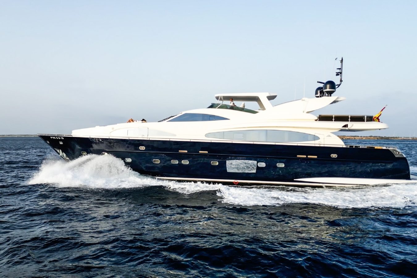 Astondoa 102 GLX My Kirios Yacht For Charter speeds across the blue ocean under a clear sky, distant shore in view.