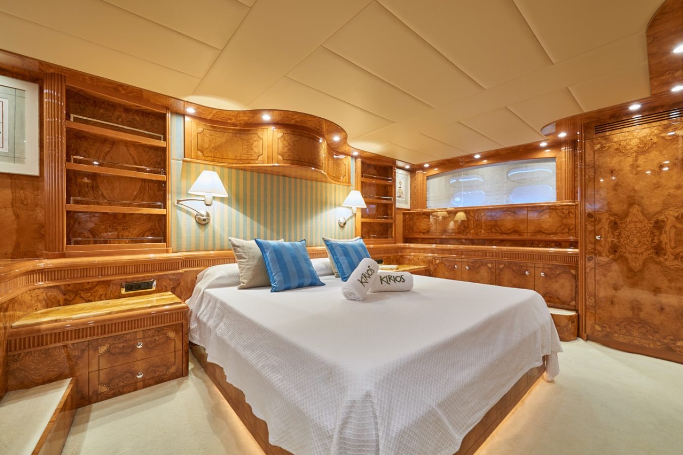 Luxurious Astondoa 102 GLX My Kirios Yacht for Charter with wood paneling, large bed, blue pillows, and rolled towels.
