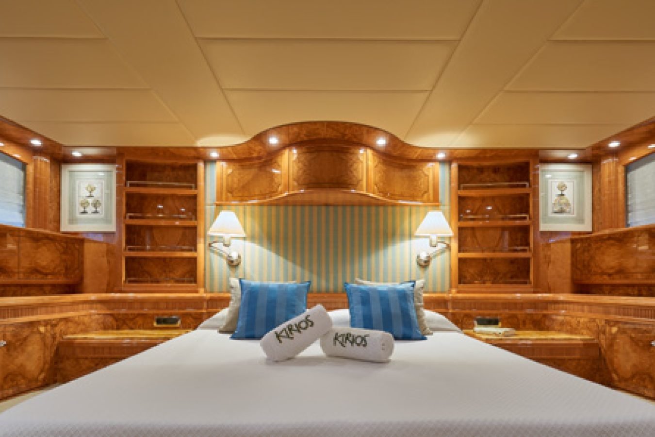 Luxurious Astondoa 102 GLX My Kirios Yacht For Charter bedroom with wood paneling, blue pillows, and round windows.