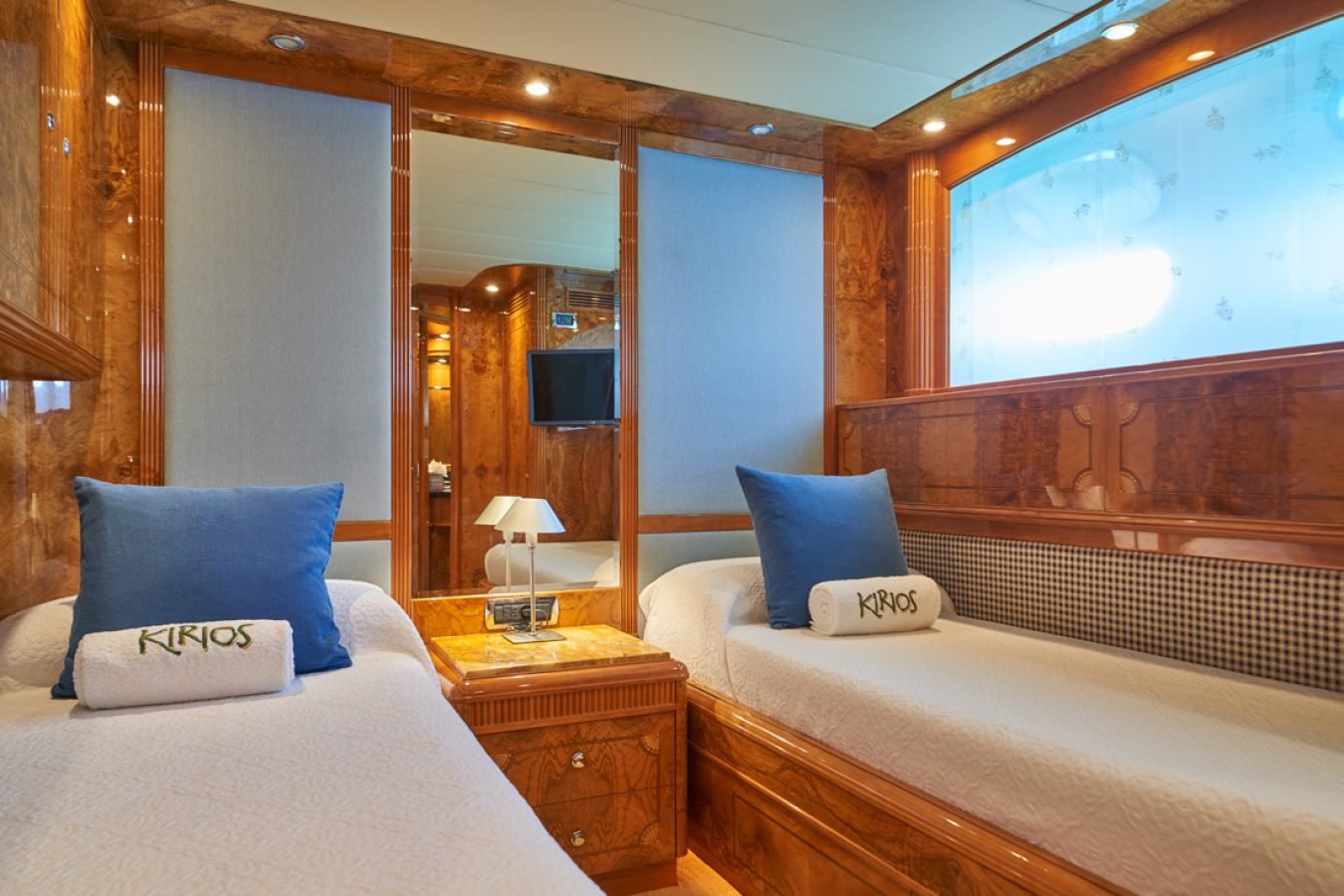 Luxurious Astondoa 102 GLX My Kirios Yacht for Charter cabin with twin beds, blue pillows, wood paneling, and TV.