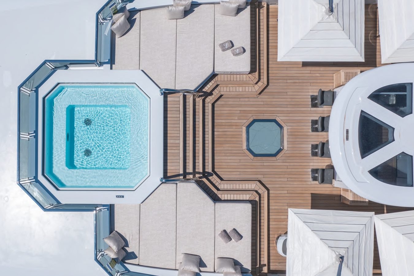 Aerial view of a yacht deck with a hexagonal pool, lounge chairs, and shaded seating on wooden flooring.