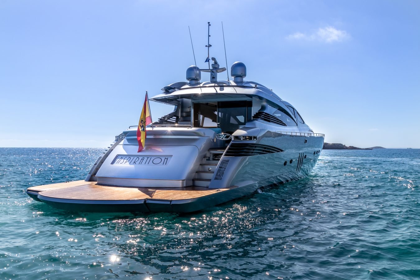 Sleek Pershing 90 Inspiration Yacht for Charter with Spanish flag, floating on clear blue water under a sunny sky.