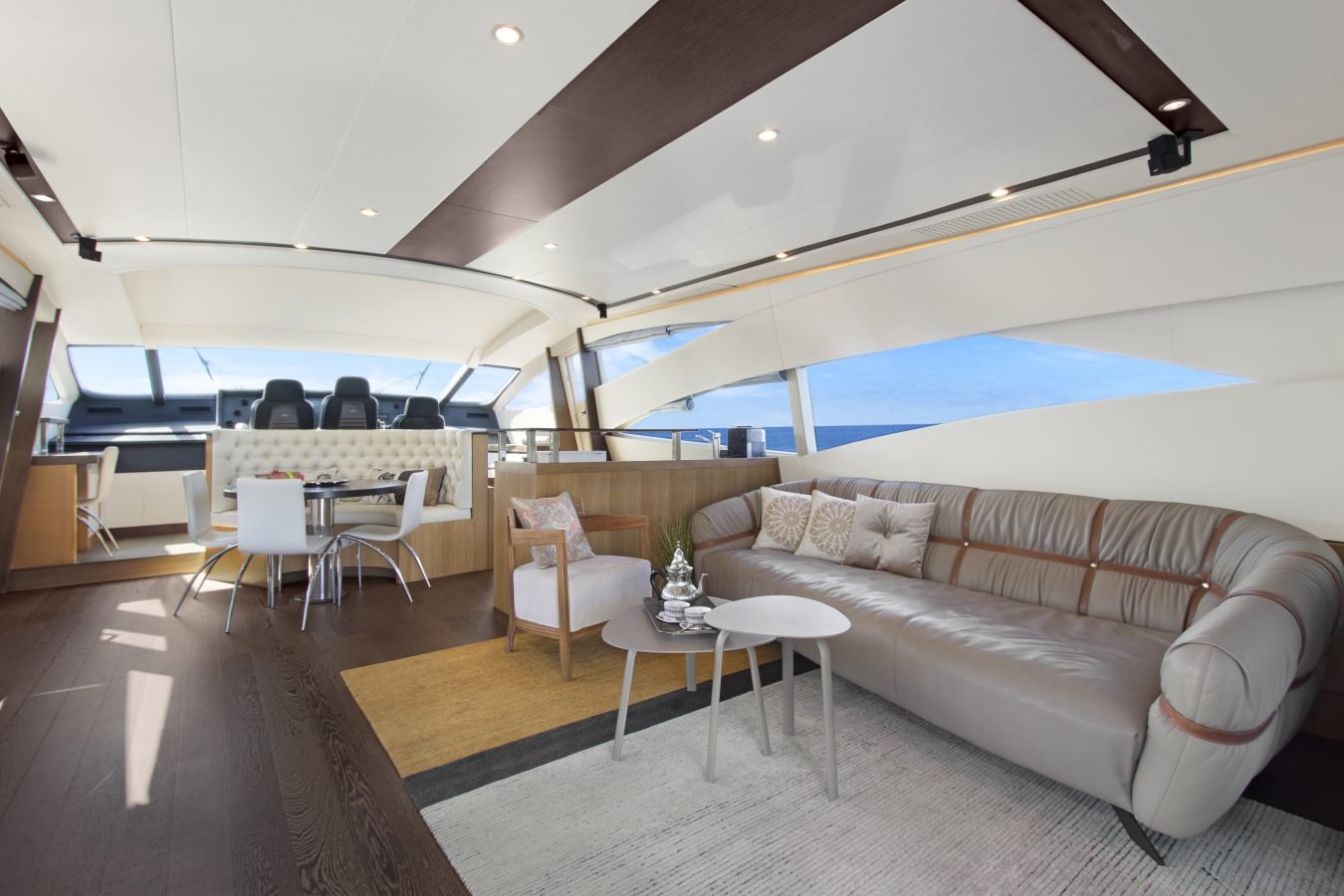 Modern Pershing 90 Inspiration Yacht For Charter features curved sofa, round table, large windows, and bright ocean views.