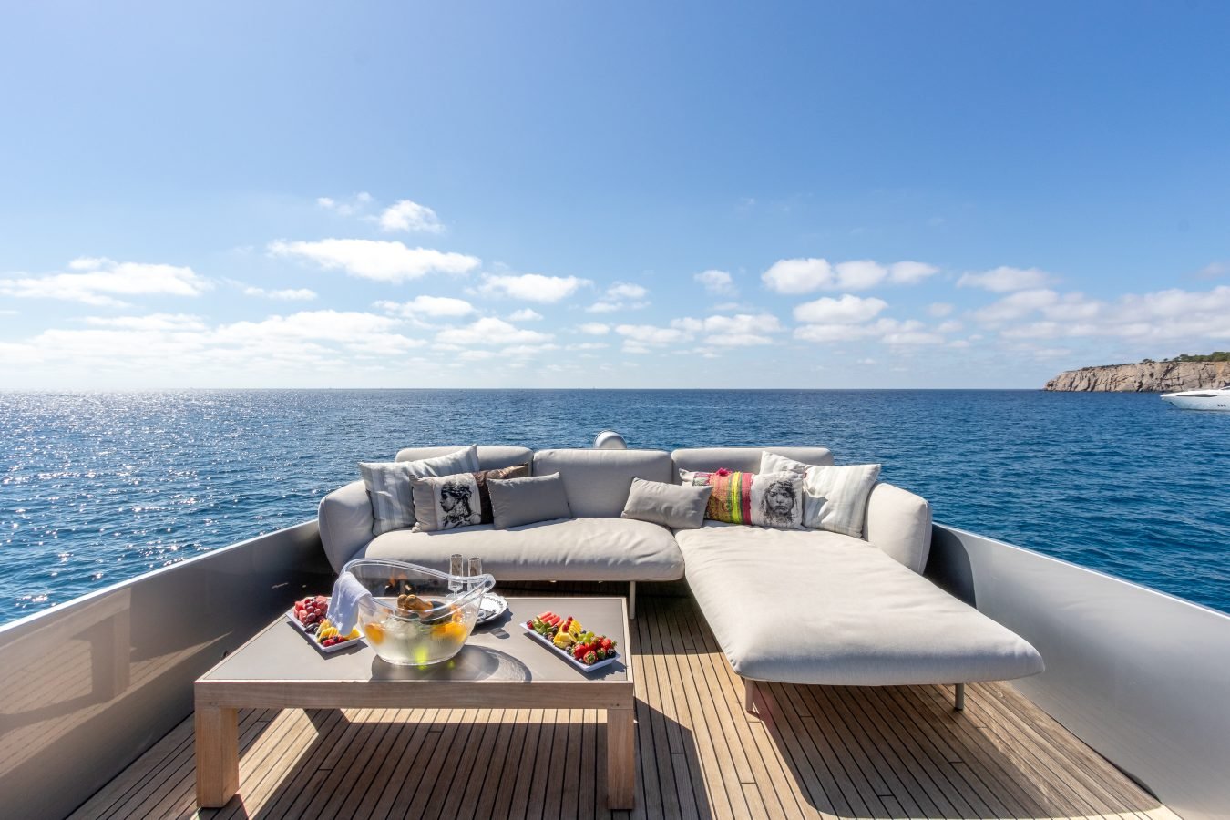 Luxurious sofa and table with snacks on Pershing 90 Inspiration Yacht For Charter, overlooking the calm blue sea.