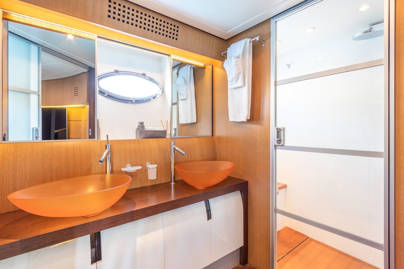 Modern bathroom like on a Pershing 90 Inspiration Yacht For Charter, with orange vessel sinks and frosted shower door.