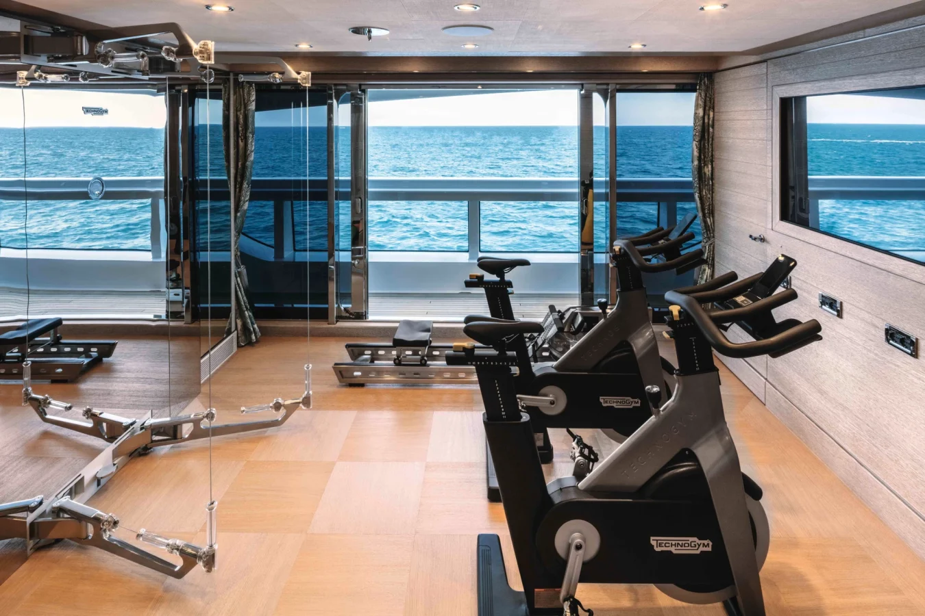 Modern gym on the CRN Starburst IV Yacht For Charter, with ocean views, bikes, strength gear, and wood floors.