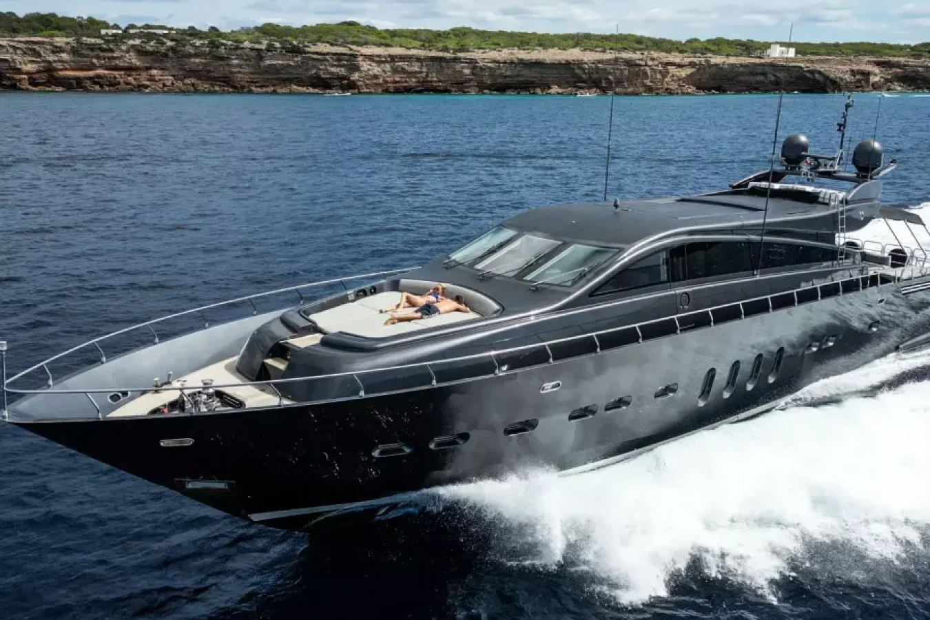 The LEOPARD 102 DARK KNIGHT Yacht speeds across blue water, a perfect yacht for charter with sunbathing on the front deck.