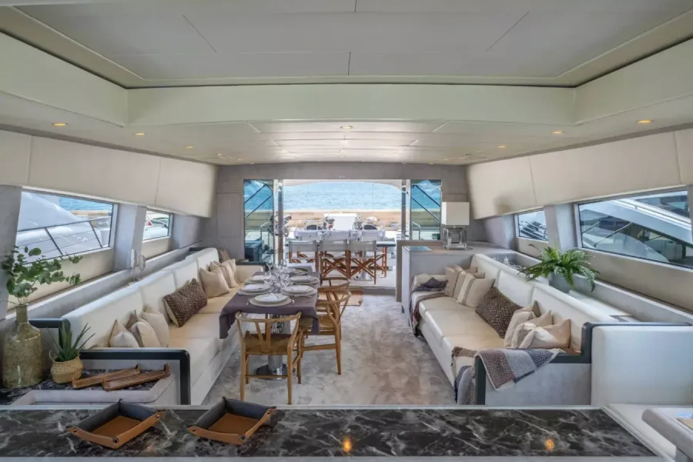 Modern LEOPARD 102 yacht interior with cream sofas, dining table, plants, large windows, and a stunning sea view.