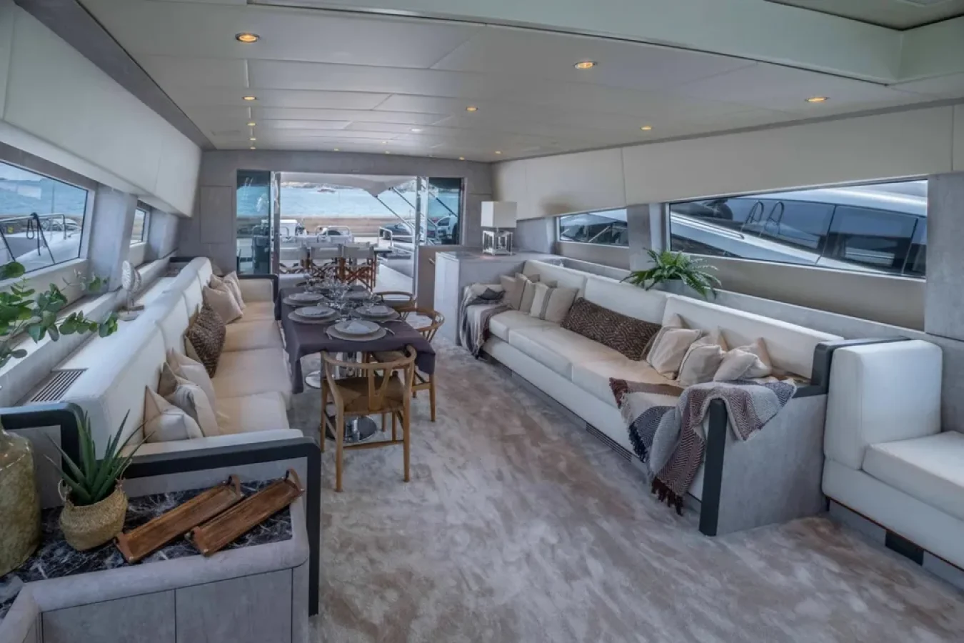 Luxurious DARK KNIGHT Leopard 102 yacht interior with beige sofas, dining table set, plants, and large windows to the sea.