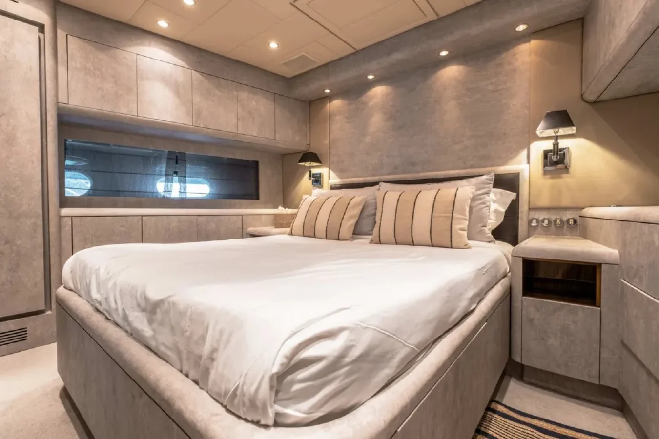 Modern bedroom with beige walls, built-ins, large bed, and striped pillows aboard the LEOPARD 102 yacht for charter.