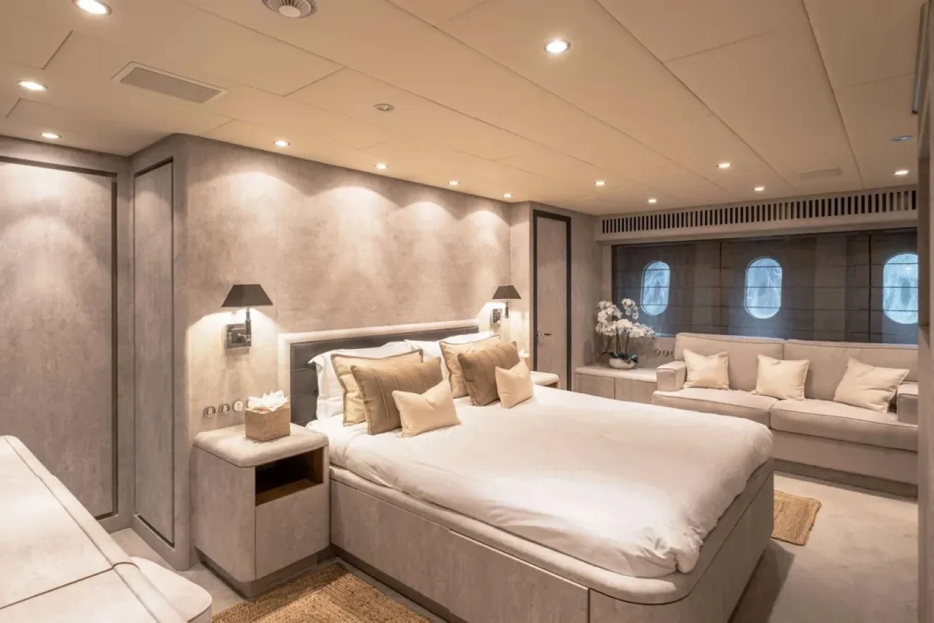 Luxurious bedroom aboard LEOPARD 102 yacht for charter, featuring a large bed, sofas, warm lighting, and beige decor.