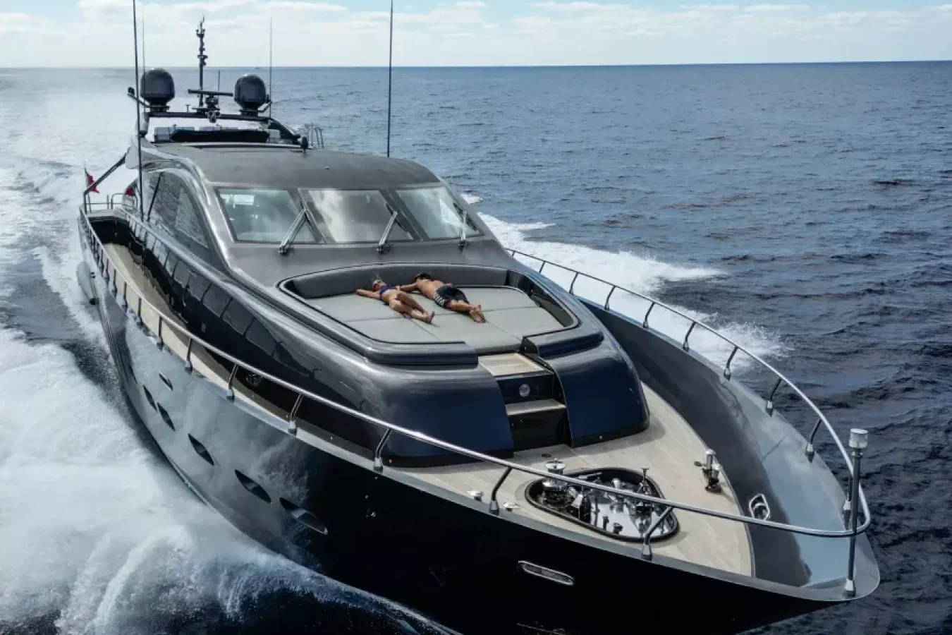 The LEOPARD 102 DARK KNIGHT yacht for charter speeds through the ocean, a guest sunbathing on its sleek front deck.