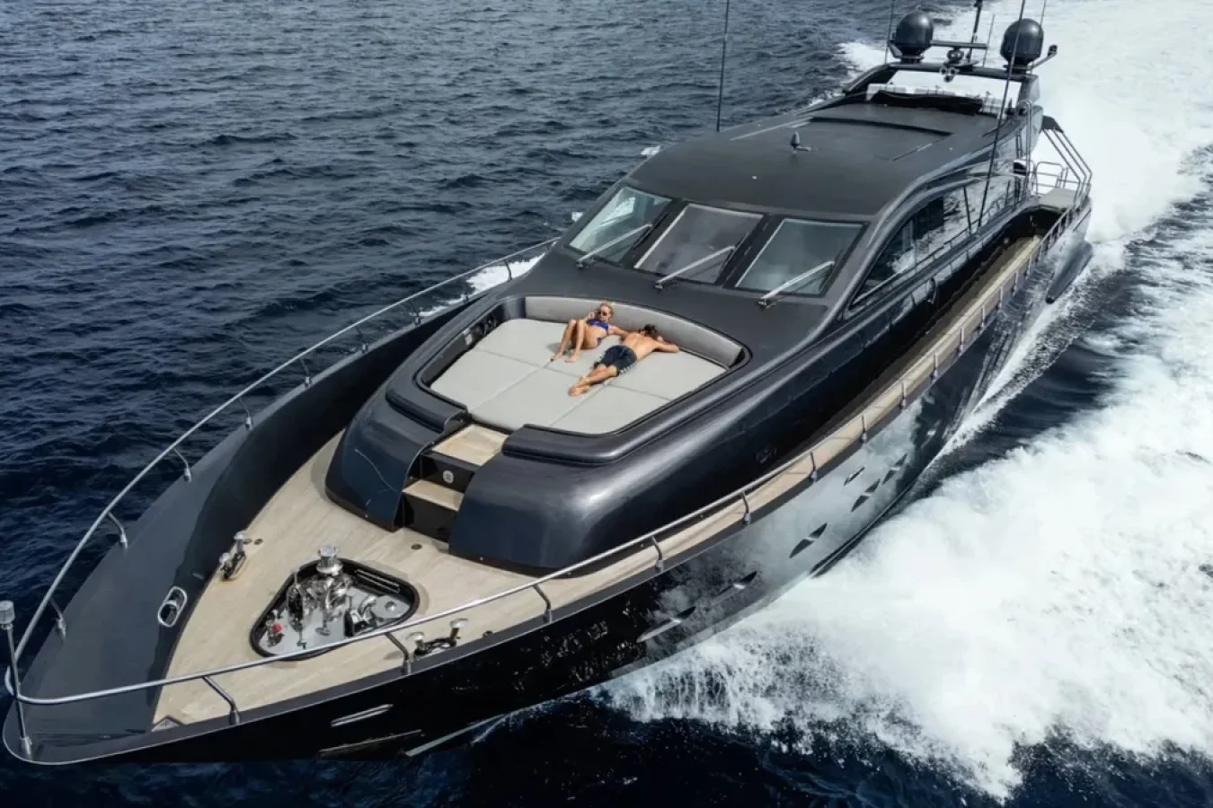 The LEOPARD 102 yacht for charter, DARK KNIGHT, speeds through blue water; someone sunbathes on the bow.
