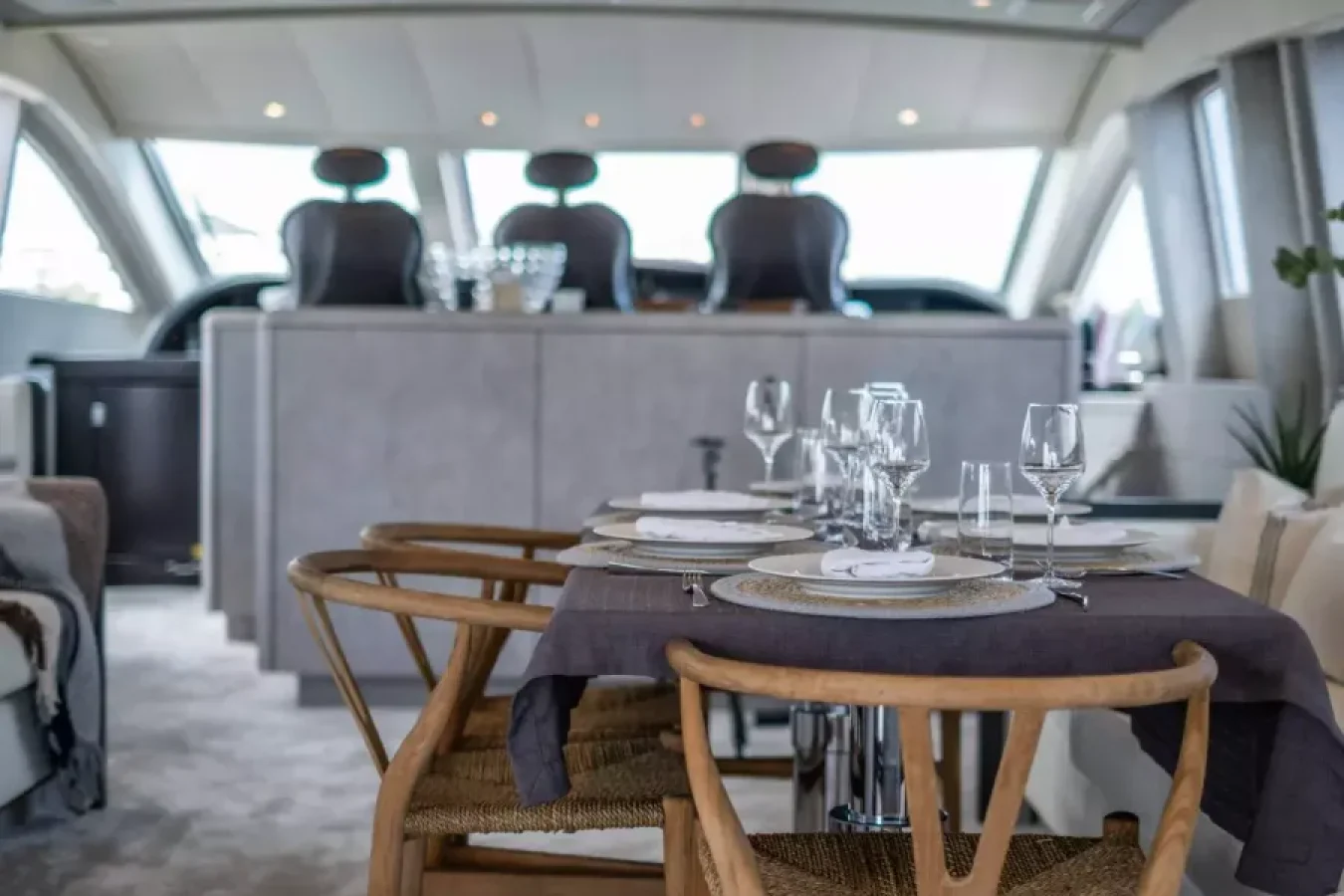 A yacht for charter, DARK KNIGHT features a formal dining table for four and wooden chairs, with the helm in view.