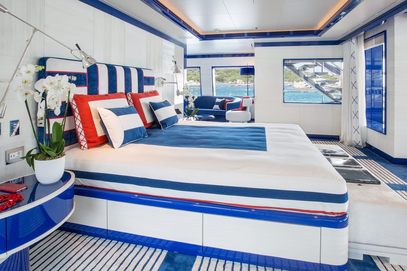 Modern yacht bedroom with a blue, white, and red color scheme, large bed, striped accents, orchids, and ocean view.
