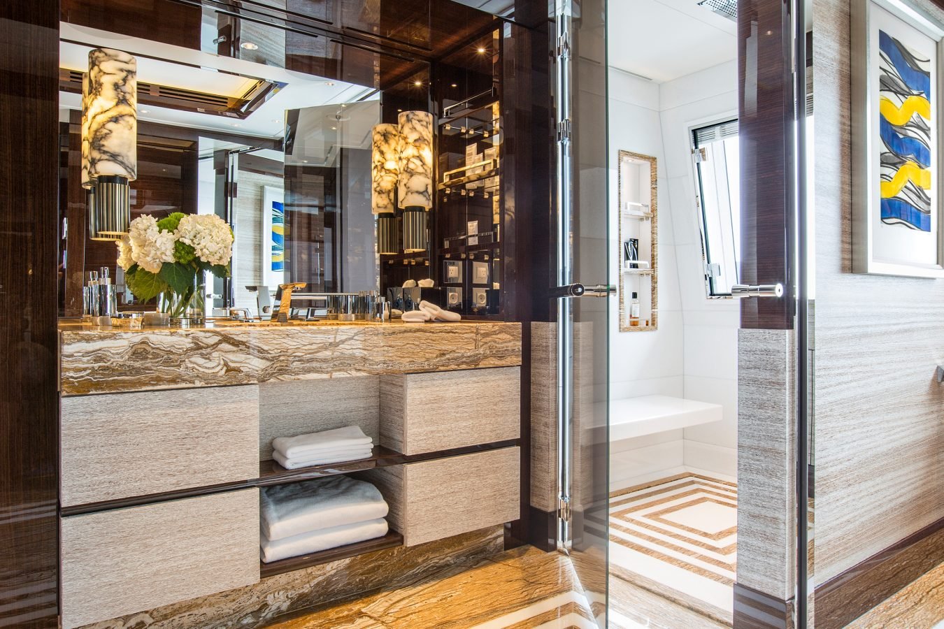 Luxurious bathroom with marble accents, double sinks, fresh flowers, and modern lighting; abstract art on the wall.