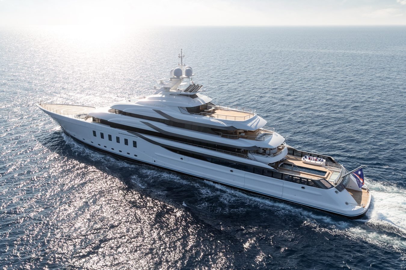 A large luxury white yacht sails on calm blue ocean water under a bright, sunny sky.