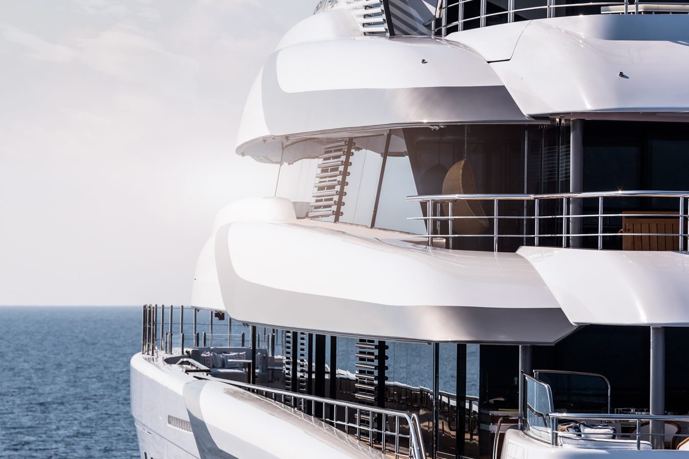A modern white luxury yacht with multiple decks is docked by calm blue ocean water under a bright sky.