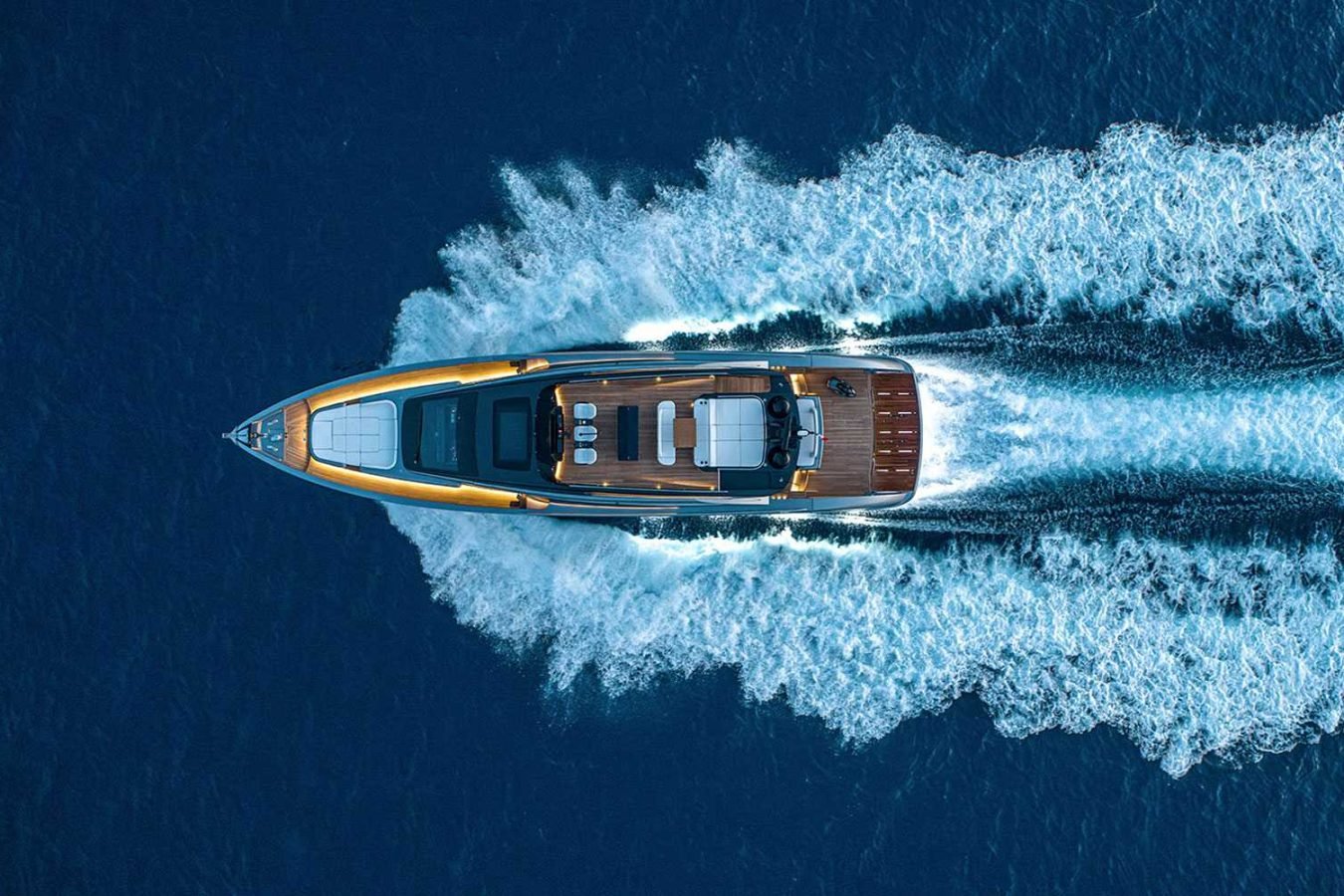 A luxury Vicky yacht speeds through deep blue water, leaving a wide, white wake behind, viewed from above.