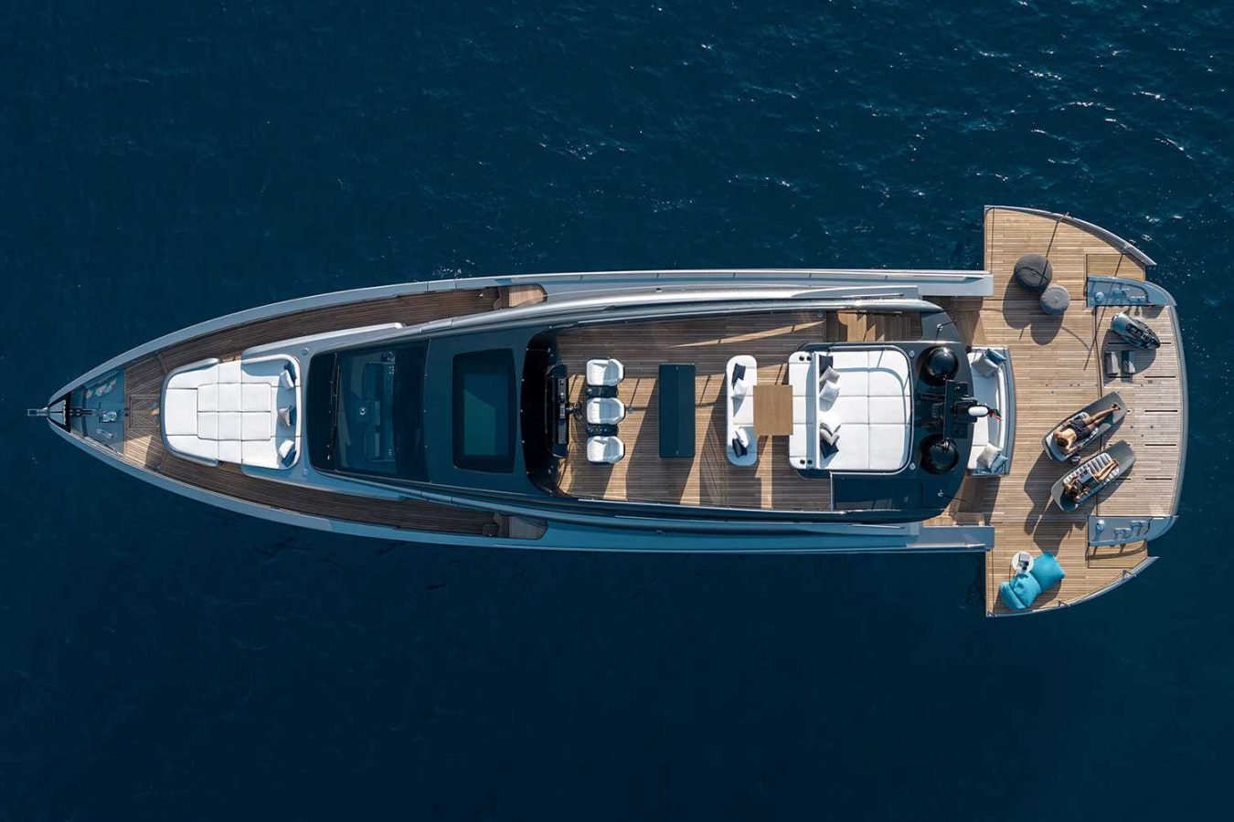 A luxury Pershing GTX80 yacht for charter, viewed from above, with sunbeds and seating on its wooden deck.