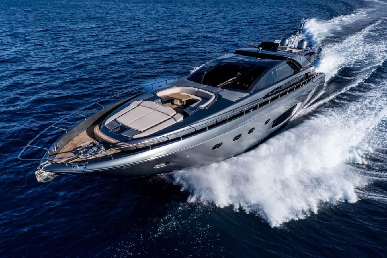 A sleek Riva 86 Tanit yacht for charter speeds across deep blue water, trailing a white wake under a clear sky.
