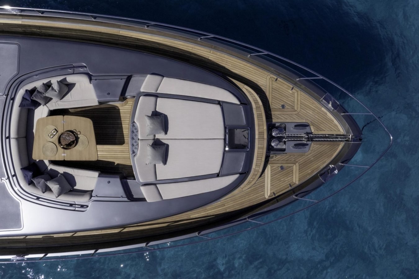Aerial view of Riva 86 Tanit’s bow with cushioned seating, table, and clear blue water—perfect yacht for charter.