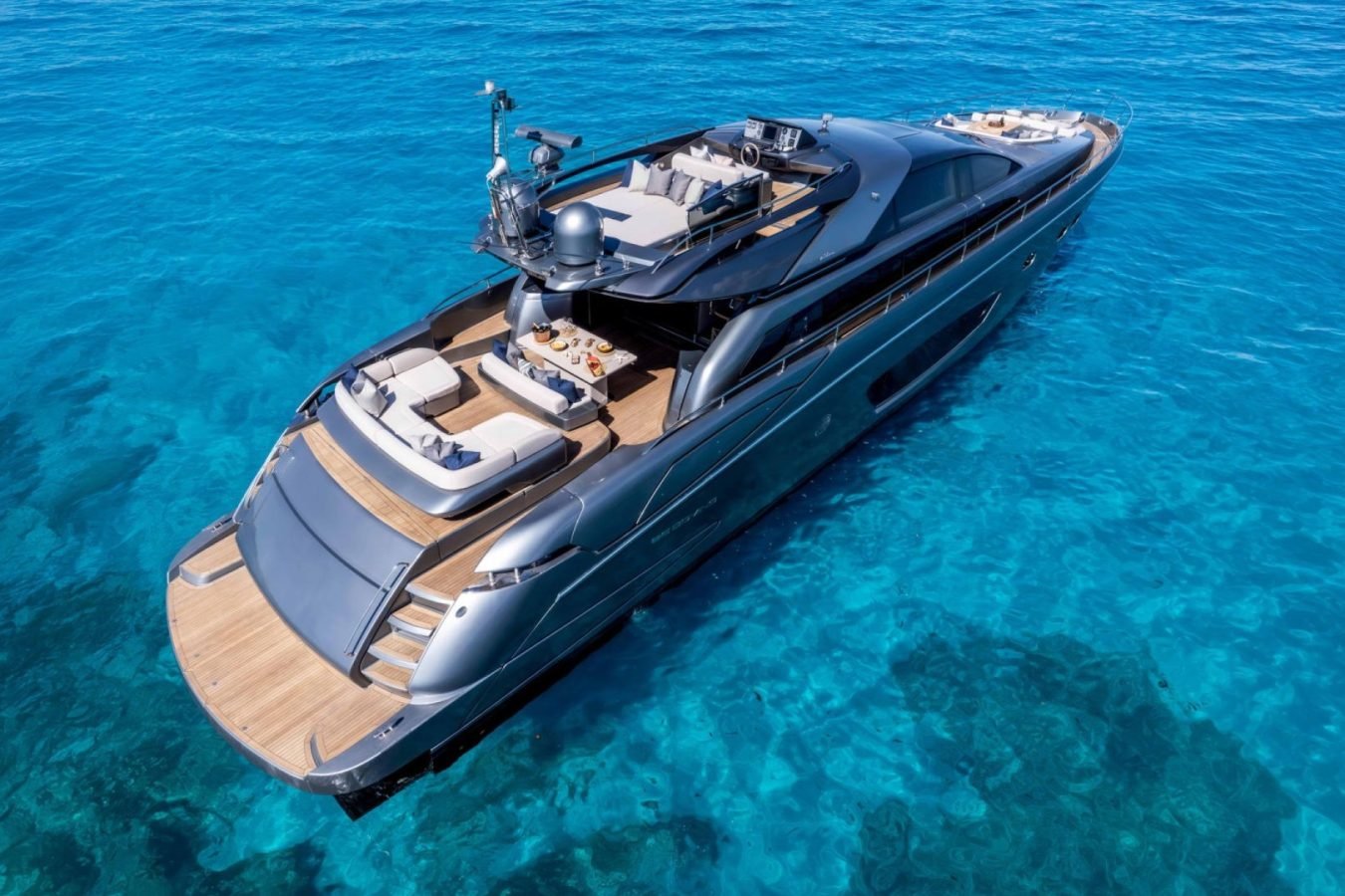 Luxurious gray Riva 86 yacht for charter on clear blue water, sun decks and seating visible, photographed from above.
