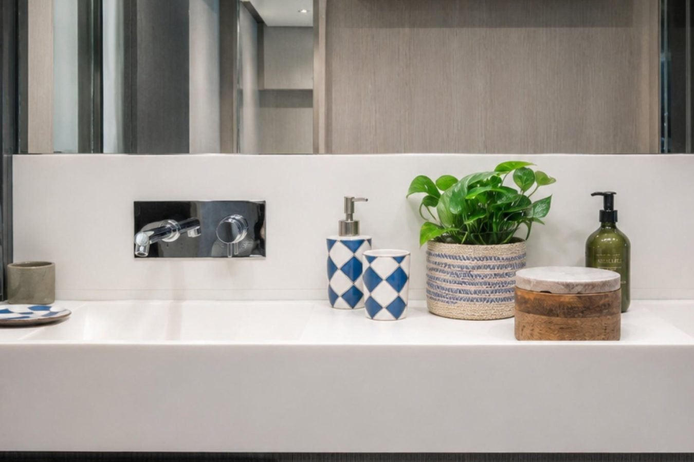 Modern bathroom sink on a Tanit Yacht with soap dispensers, plant, wooden container, and cup on a white counter.