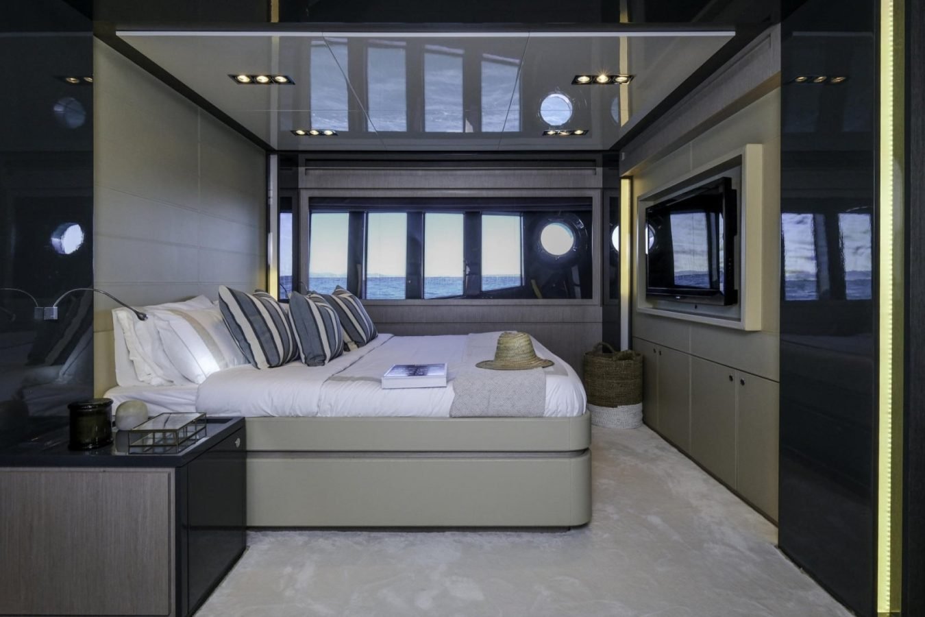 Modern yacht bedroom on Riva 86 Tanit with striped pillows, TV, basket, and ocean views—perfect for a yacht charter.