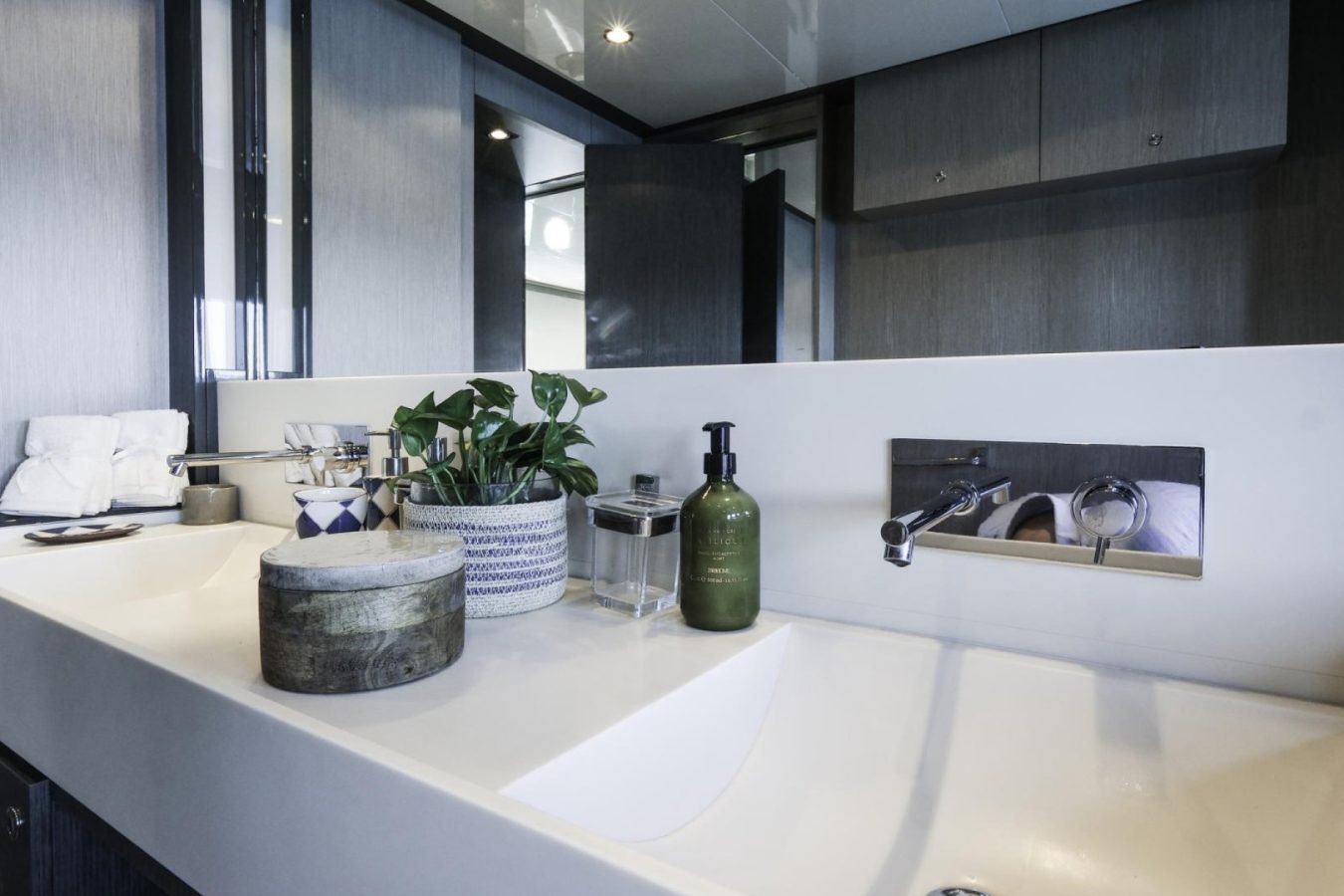 Modern bathroom reminiscent of a Riva yacht, with double sinks, lush plants, and a mirror reflecting dark cabinets.
