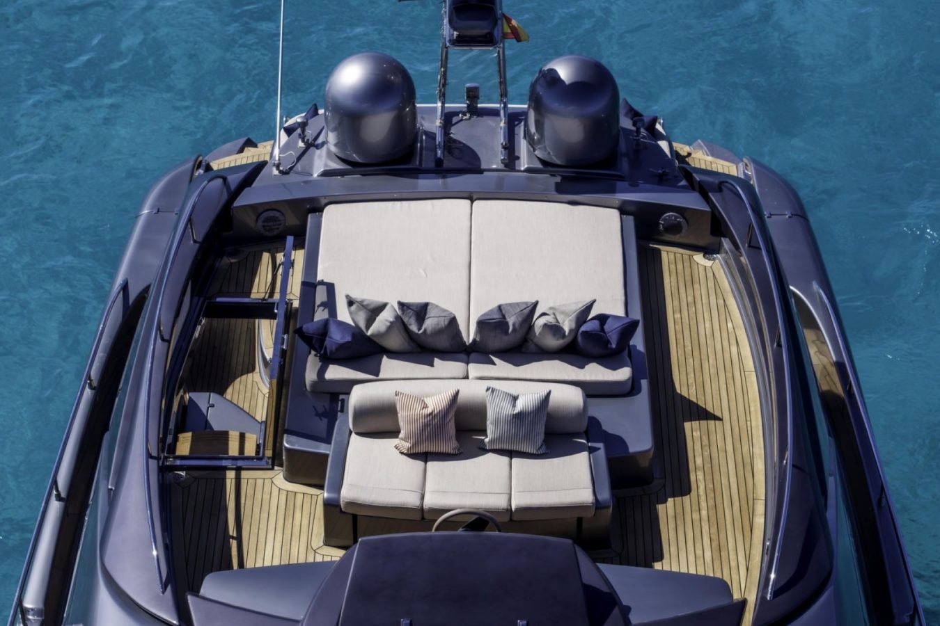 A luxury yacht charter’s upper deck, like the Riva 86 Tanit, boasts sun loungers and wood floors over clear blue water.
