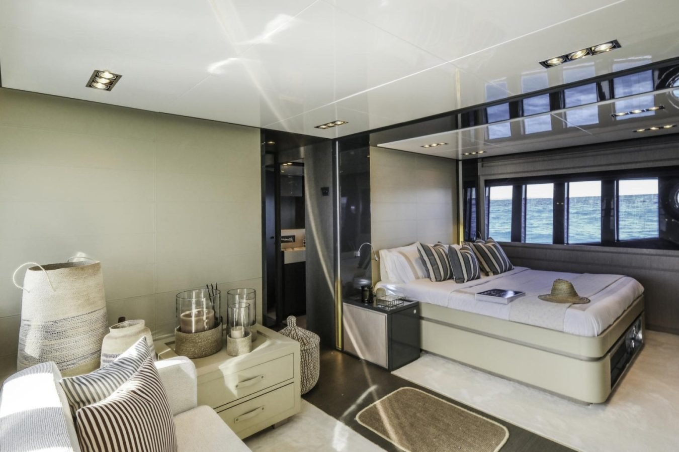 Modern Riva 86 Tanit yacht bedroom with large windows, striped pillows, sofa, baskets, and stunning ocean view outside.