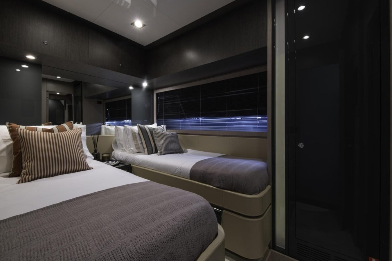 Two twin beds, gray bedding, striped pillows—cozy style aboard the Riva 86 Tanit yacht for charter.