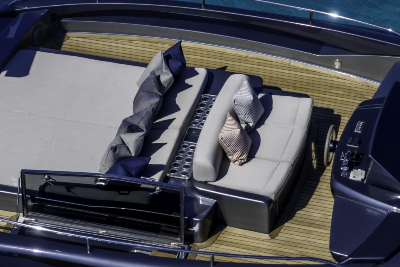 A yacht charter deck with gray lounge beds, striped pillows, and a control panel, all aboard the luxury yacht Riva 86 Tanit.