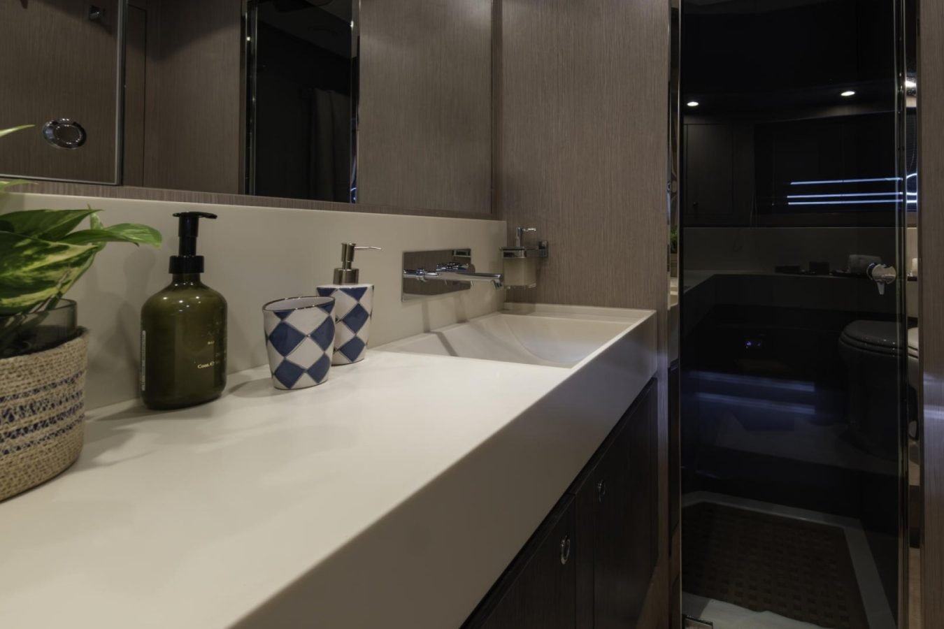Modern bathroom on Riva 86 Tanit yacht for charter, featuring a plant, long sink, and dark toilet area in the background.