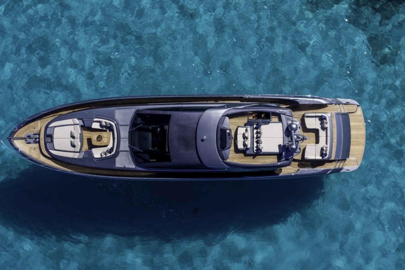 A luxury Riva 86 Tanit yacht for charter floats on clear blue water, showing deck seating and sunbathing areas.