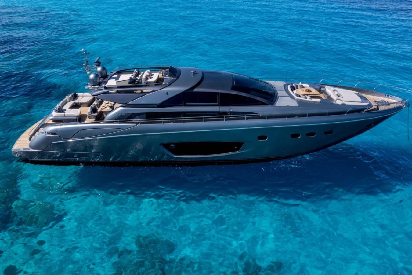A sleek Riva 86 Tanit yacht floats on vibrant blue water, casting a sharp shadow—perfect for luxury yacht charter dreams.