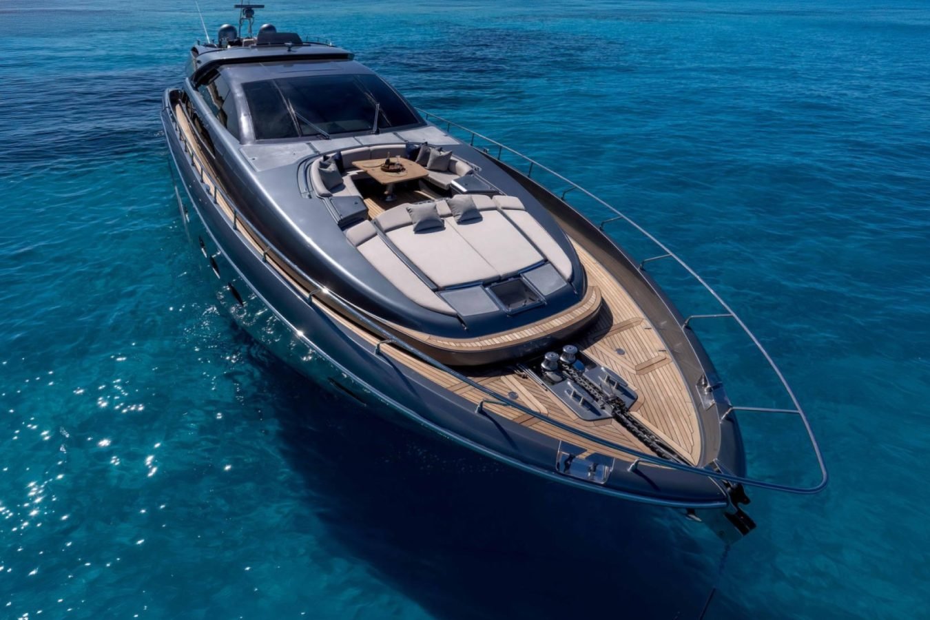 A Riva 86 Tanit yacht for charter floats on clear blue water, its sun deck shining under bright sunlight, viewed from above.